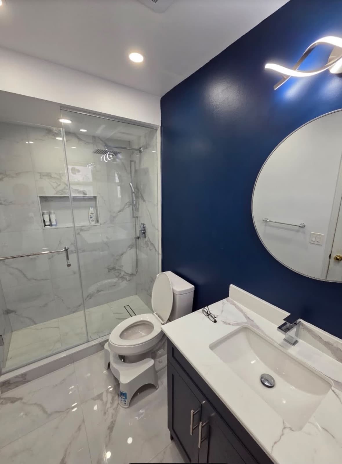 Finished bathroom with glass shower, marble-look tile and navy feature wall