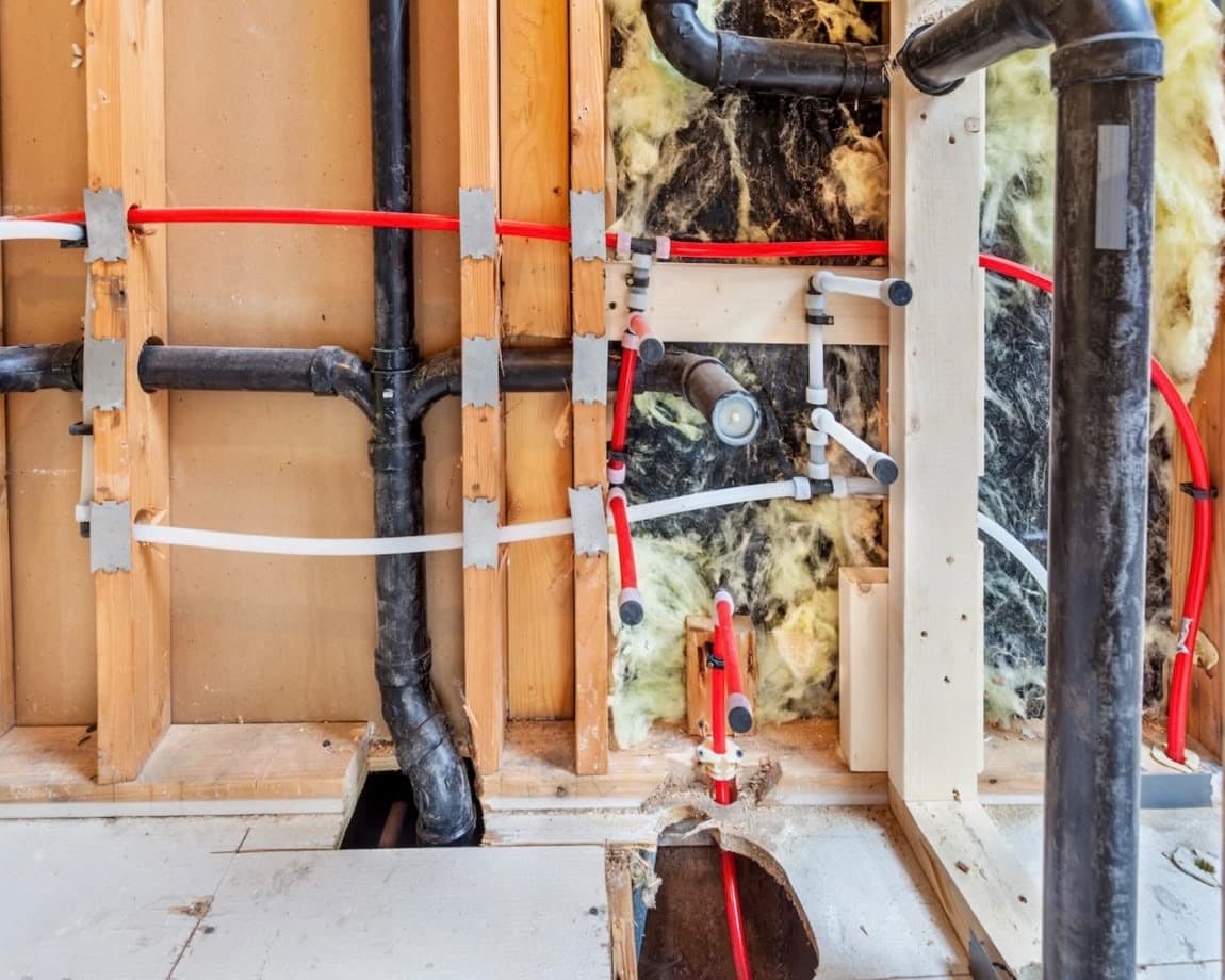 Bathroom rough-in with black drain and vent pipes and red and white PEX supply lines in an open wall